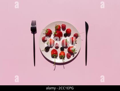 Fresh berries, strawberries, raspberries, blackberries in pink ceramic plate on pink background. Vegetarian or fruitarian diet concept. Stock Photo