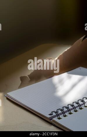 Open spring-bound notebook in sunlight. New diary with blank pages on torn wrapping paper. Side view at an angle. Selective focus. Stock Photo