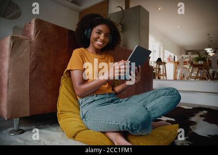 Low angle portrait view of beautiful young woman watching video at home using digital tablet with wireless headphones Stock Photo