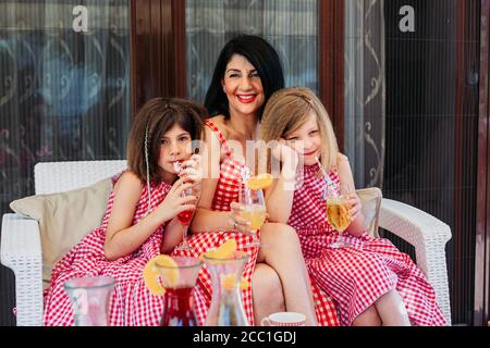 Young mom sitting with her two little daughters drinking juice Stock Photo