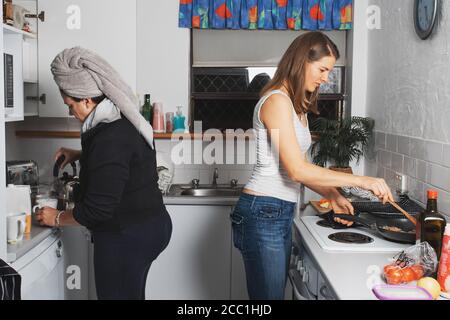 Two middle-aged women are cooking dinner, talking and laughing in a kitchen Stock Photo