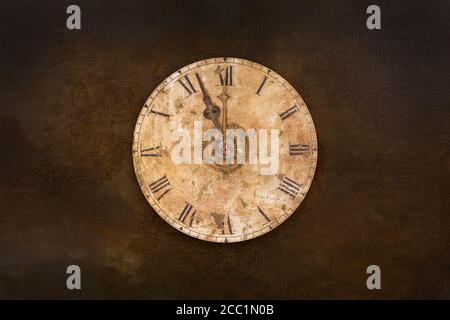 Vintage and heavily weathered clock face with time set to a few minutes to twelve o clock in front of a dark brown background Stock Photo