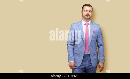 Portrait of well dressed Caucasian young man. Handsome young man with lowered hands looking at camera with smile while standing on light peach backgro Stock Photo