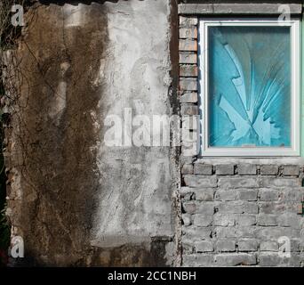 A broken window on a brick wall beside an old painted concrete wall Stock Photo