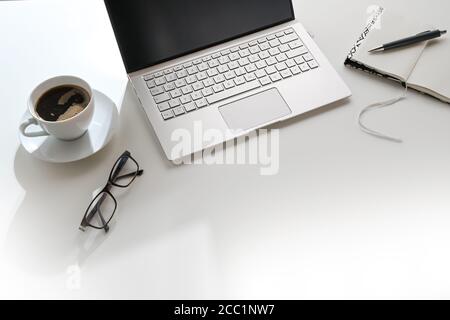 White office desk in sunlight from the back with laptop, notepad and a coffee cup, workplace in a modern company or at home, copy space, selected focu Stock Photo