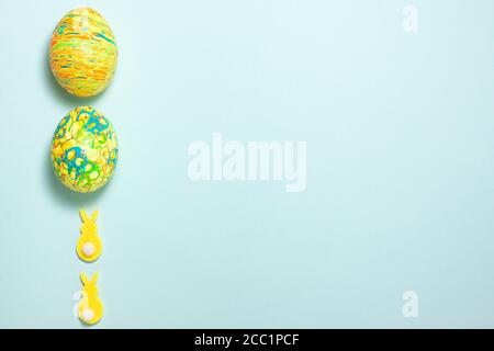 Yellow rabbits and green easter egg on the left side on blue background. Flat lay top viiew with copy space Stock Photo