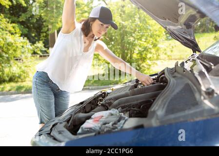 A woman waits for assistance near her car broken down on the road side. Stock Photo