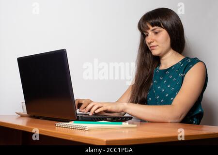 A woman sits at a desk and prints on the keyboard of a laptop. Stock Photo