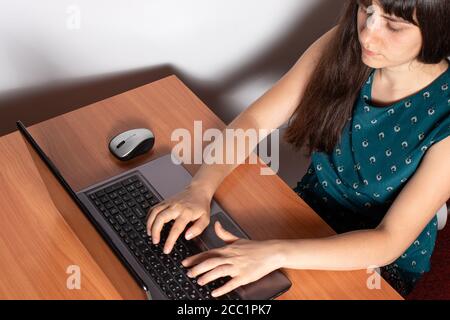 A woman sits at a desk and prints on the keyboard of a laptop. Stock Photo