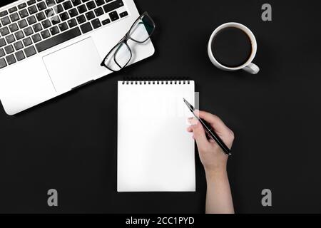 hand holds pen over notebook on black table near laptop. Stock Photo
