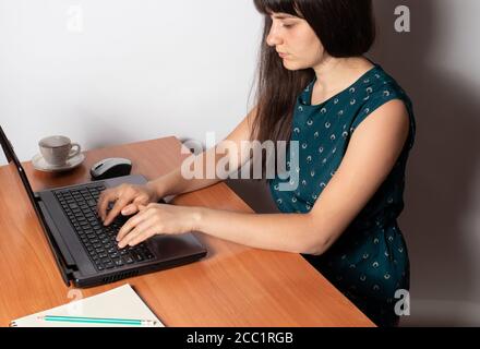 A woman sits at a desk and prints on the keyboard of a laptop. Stock Photo