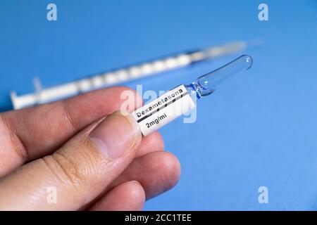 A hand holding a dose of dexamethasone, write in portuguese language, on blue background. Stock Photo