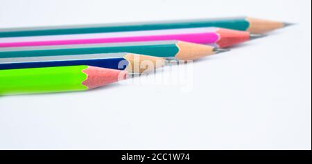 Five different colored wood pencil crayons placed beside one another on white paper background Stock Photo
