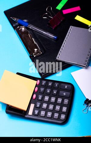 Business card with binder near sticky notes and grey notebook. Bookmarks of different colors near pen and black clip folder on cyan background. Business accessories concept. Stationery and calculator Stock Photo