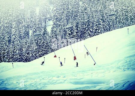 Austria - Skiers on a sky slope bordered by fir trees on the Tauern Alps,with cable cars passing over Stock Photo