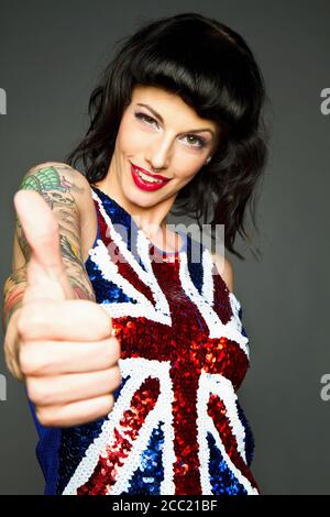 Young woman showing her thumb with tatto on her hand against grey background, portrait, smiling Stock Photo