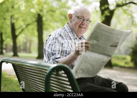 Germany, North Rhine Westphalia, Cologne, Senior man reading newspaper on bench in park Stock Photo