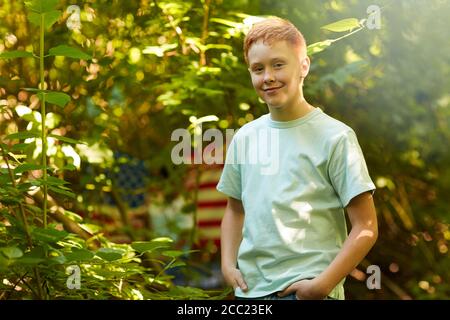 Waist up portrait of red-haired teenage boy smiling at camera while standing outdoors in forest or back yard, copy space Stock Photo