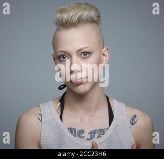 A young woman with a shaved head and tattoos on her shoulder, arms and ...