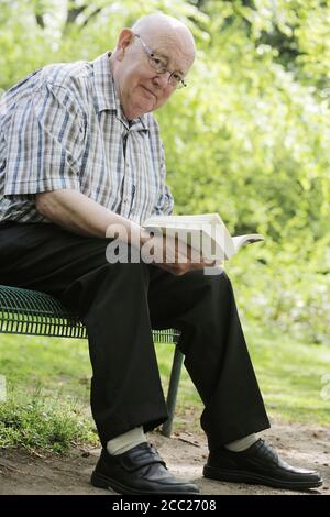 Germany, Cologne, Portrait of senior man reading book on park bench Stock Photo