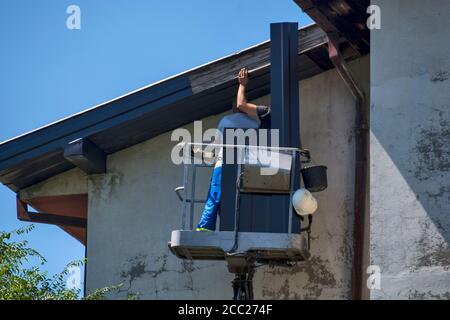 Two masters are replacing the sheets on the sides of a tall building. Works are performed from a special basket at high altitudes. Stock Photo
