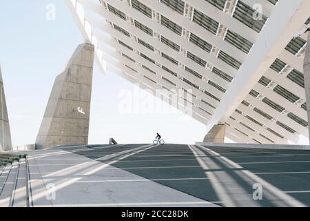 Distant anonymous person riding bike under modern solar panel on city street Stock Photo