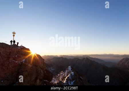 Germany, Bavaria, Bavarian Alps, Wetterstein Range, View of cross on summit of Zugspitze with hikers at sunrise Stock Photo