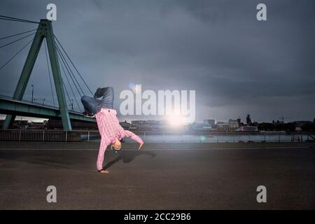 Germany, Cologne, Young man performing breakdance, Rhine bridge in background Stock Photo