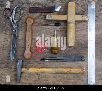 Leather craft tools on a old wood backgrounde. Craftsman work desk . Piece of hide and working handmade tools on a work table. Stock Photo