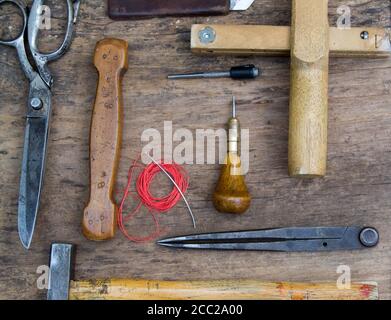 Leather craft tools on a old wood backgrounde. Craftsman work desk . Piece of hide and working handmade tools on a work table. Stock Photo