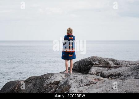 woman standing on rocks wrapped in a Pendleton blanket in Sweden Stock Photo