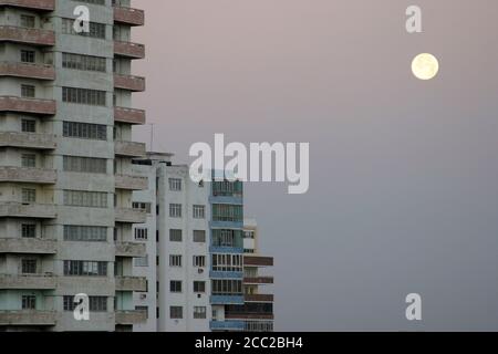 old living blocks in front of a dull gray sky with a full moon, Havana, Cuba Stock Photo