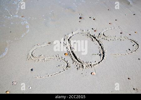 SOS - word drawn on the sand beach with the soft wave. Stock Photo