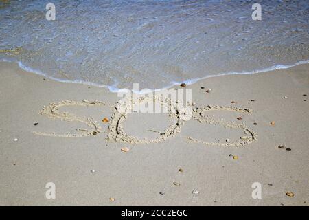 SOS - word drawn on the sand beach with the soft wave. Stock Photo