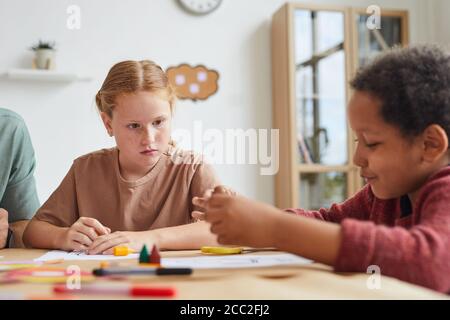Portrait of freckled red haired girl looking at friend while drawing pictures together during art class in school, copy space Stock Photo