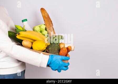 Safe food delivery or donation concept. Food delivery or shopping during coronavirus quarantine. Girl in disposable gloves holding Box with food ingre Stock Photo