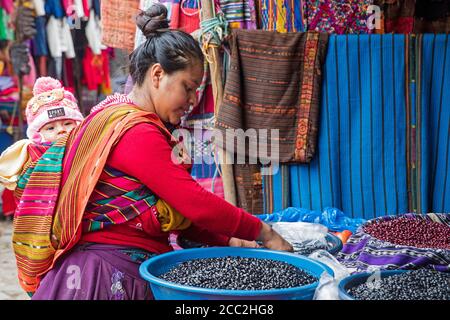 Local Mayan K'iche woman with child on her back selling beans on market day in the town Chichicastenango, El Quiché, Guatemala, Central America Stock Photo