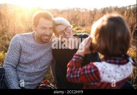 Small girl with family on picnic in autumn nature, taking photographs with camera. Stock Photo