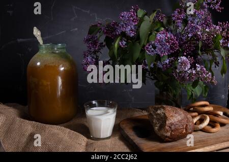 Rural still life with lilacs, milk, honey and bread. Bouquet of lilacs and honey with milk. Low key. Stock Photo