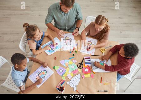 Above view at multi-ethnic group of kids drawing pictures of space rockets with crayons while enjoying art and craft class in pre school or developmen Stock Photo