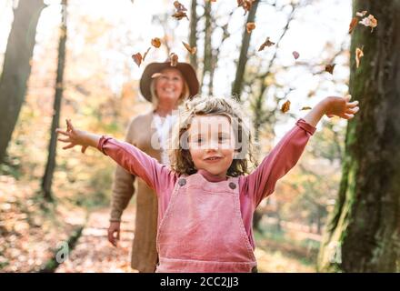 Small girl with grandmother on a walk in autumn forest, having fun.