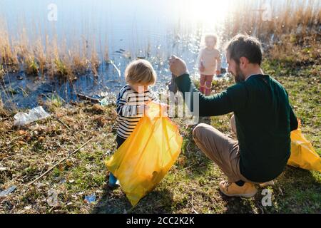 Father with small kids collecting rubbish outdoors in nature, plogging concept. Stock Photo