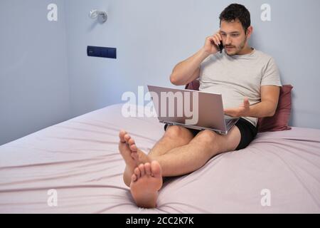 Young adult talking with someone and discussing about something that he is watching on the laptop. Working from home concept. Stock Photo