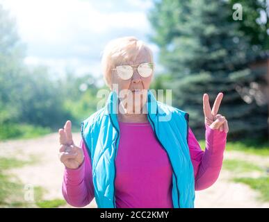 Happy, fashionable 90-year-old grandmother with gray hair, sunglasses and a smile in nature on a Sunny summer day.. Stock Photo