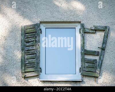 Close-up of an old window with green wooden shutters on an orange broken wall. Stock Photo