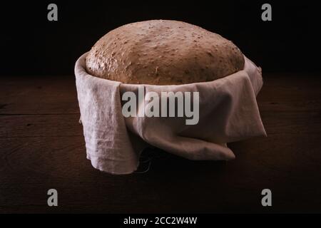 Homemade unbaked dough loaf, raw in proofing basket on rustic wooden table,  ready to bake, common flour with wholemeal artisan bread Stock Photo