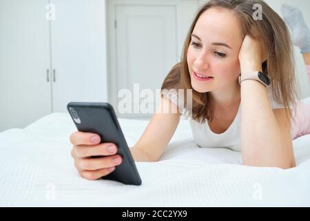 Beautiful young woman lying on the bed and looking at her smartphone Stock Photo