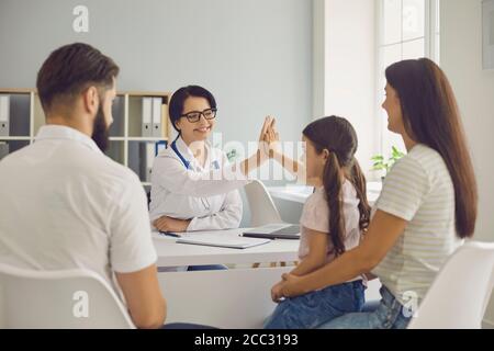 Young smiling woman doctor giving high five to girl patient with family in clinic Stock Photo