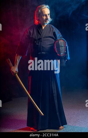 mature caucasian kendo fighter in traditional dress outfit stand with shinai in hands, going to fight with enemy, posing at camera isolated over color Stock Photo