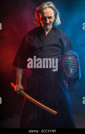 mature caucasian kendo fighter in traditional dress outfit stand with shinai in hands, going to fight with enemy, posing at camera isolated over color Stock Photo